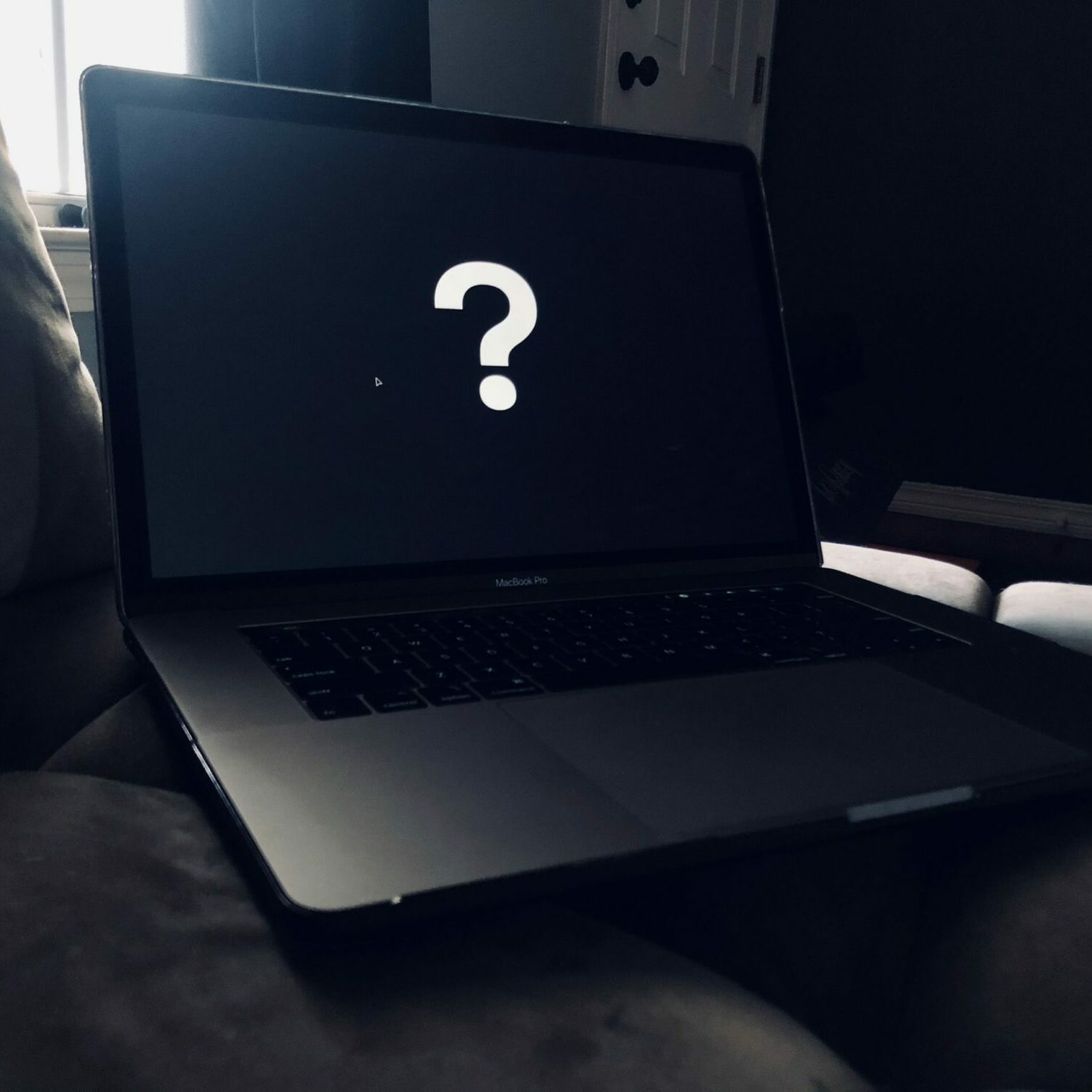 Photo of a laptop with a black screen and a large white question mark