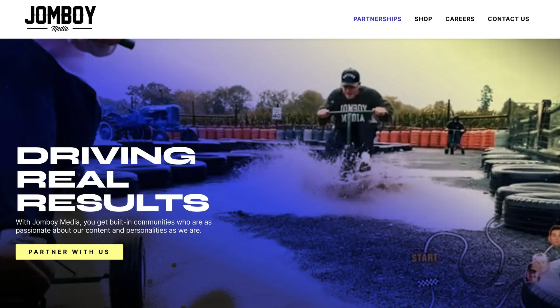 A dynamic website banner for jomboy media featuring a man skateboarding through a puddle, splashing water, with the text "driving real results" prominently displayed.